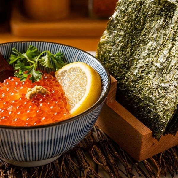 A bowl of bright orange salmon roe with a lemon slice and nori seaweed sheets.