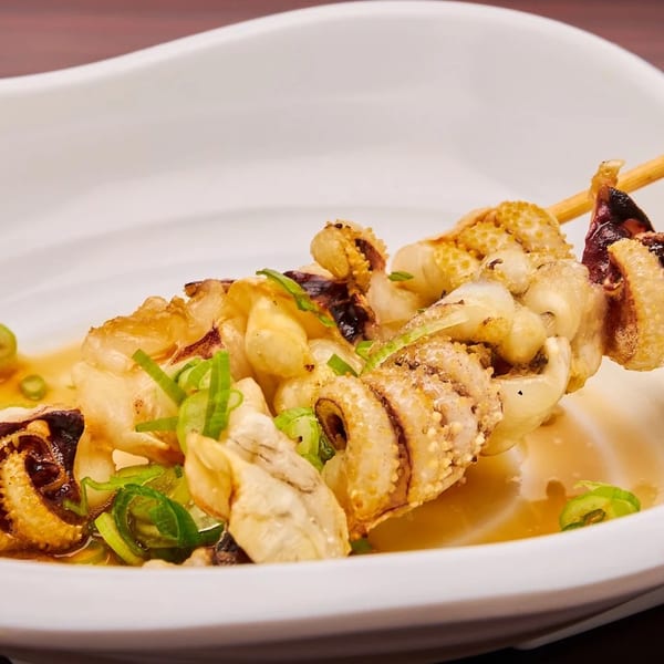 Grilled squid skewers with green onions and sauce on a white plate.